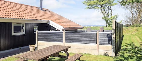 Une maison avec un toit en tuiles, une terrasse en bois et une cour clôturée.