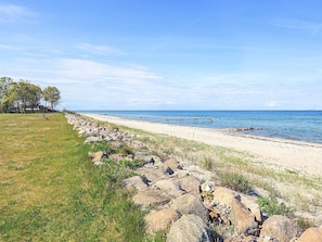 A beach with a rocky shoreline, a wooden pier, and a grassy area with trees. - 4 Star Holiday Home in Otterup (Otterup)