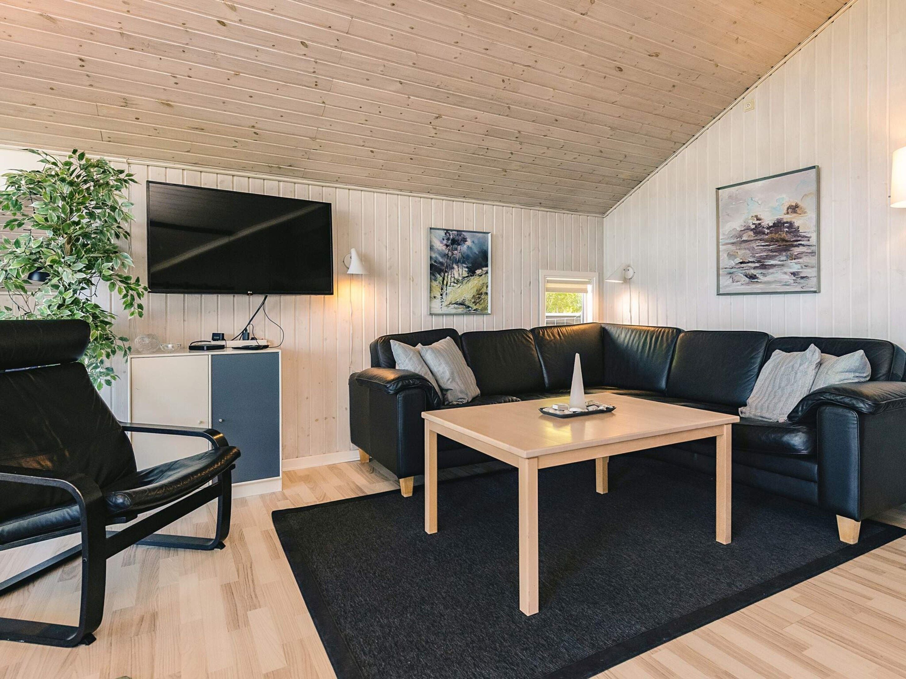A modern living room with a flat-screen TV, a black leather sofa, a wooden coffee table, and a black rug.
