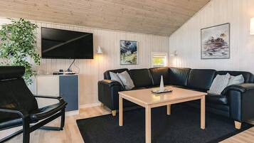 A modern living room with a flat-screen TV, a black leather sofa, a wooden coffee table, and a black rug.