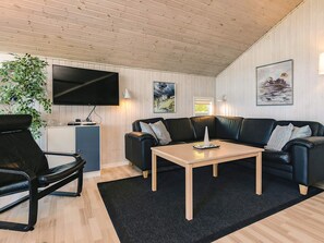 A modern living room with a flat-screen TV, a black leather sofa, a wooden coffee table, and a black rug. - 4 Star Holiday Home in Otterup (Otterup)