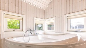Une salle de bain moderne avec une baignoire sur pieds, des murs en bois et des fenêtres donnant sur un paysage verdoyant.