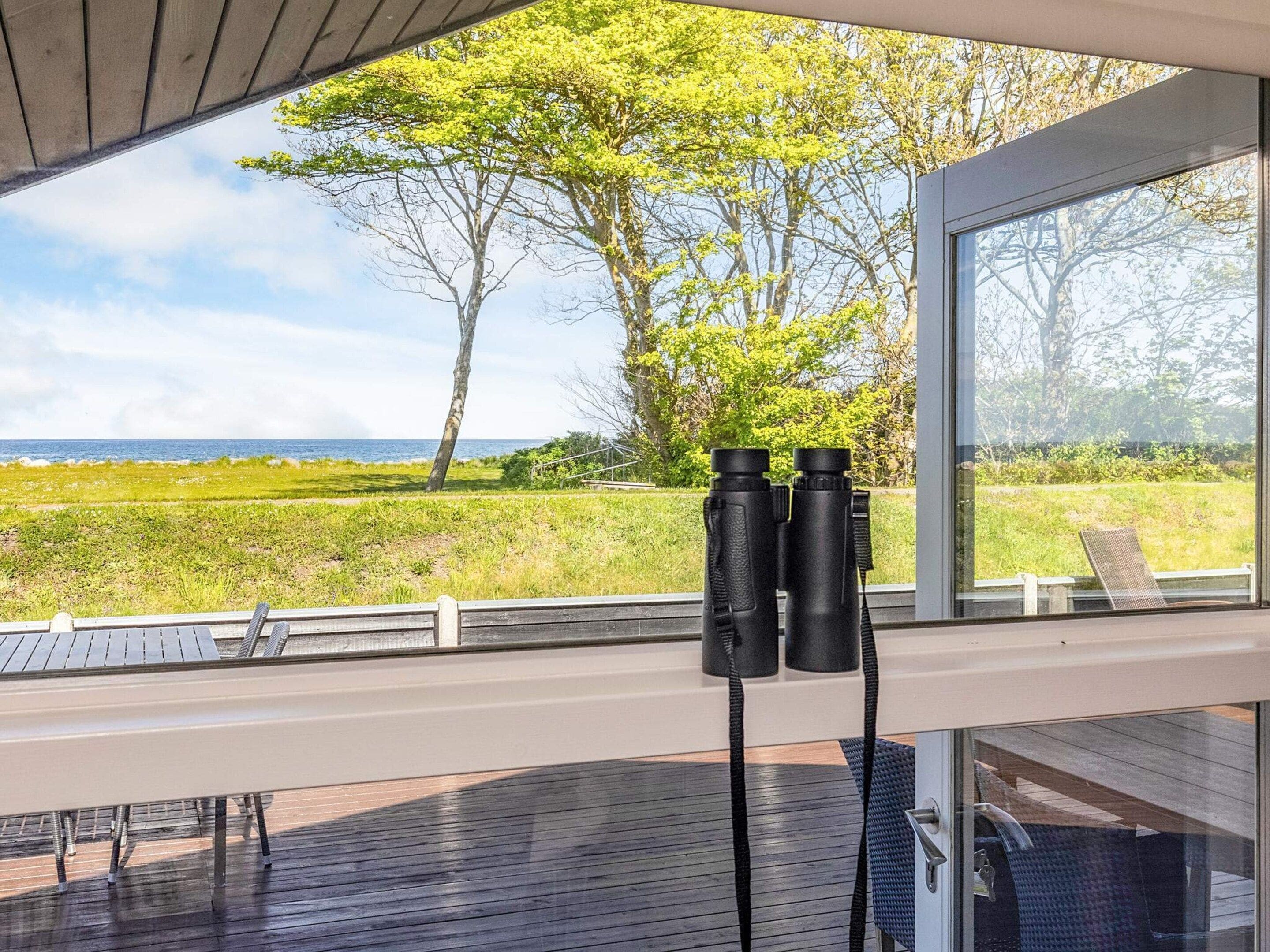 A deck with binoculars, a chair, and a view of the sea and trees.