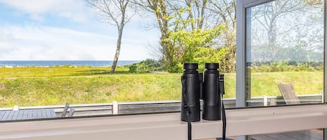 A deck with binoculars, a chair, and a view of the sea and trees.