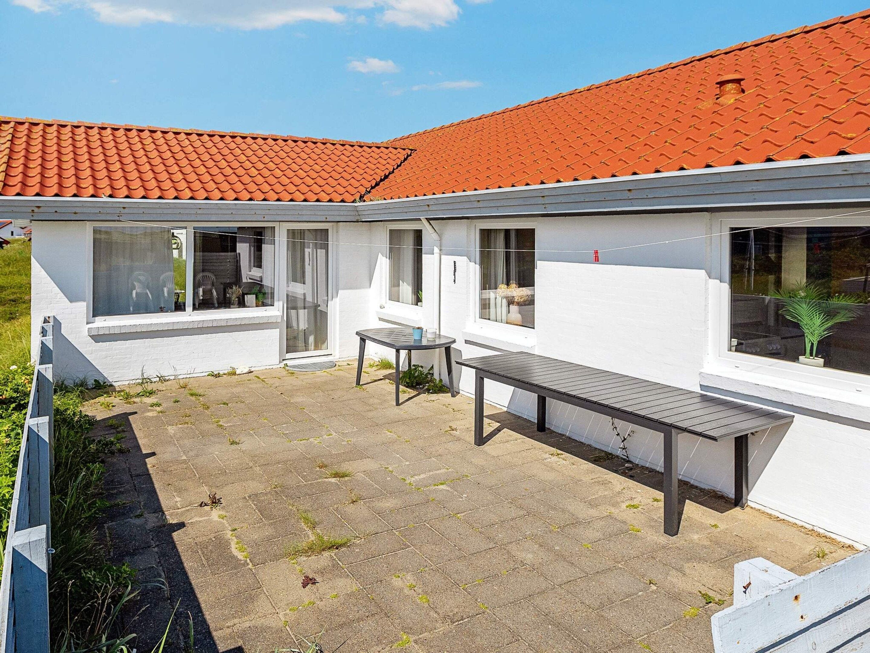 Una casa moderna con techo de tejas rojas, un patio con mesa y sillas, y fachada blanca.