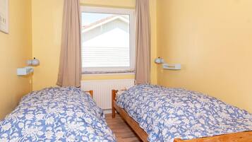 Ein Schlafzimmer mit zwei Holzbetten, einem Fenster mit Vorhängen und Nachttischlampen.
