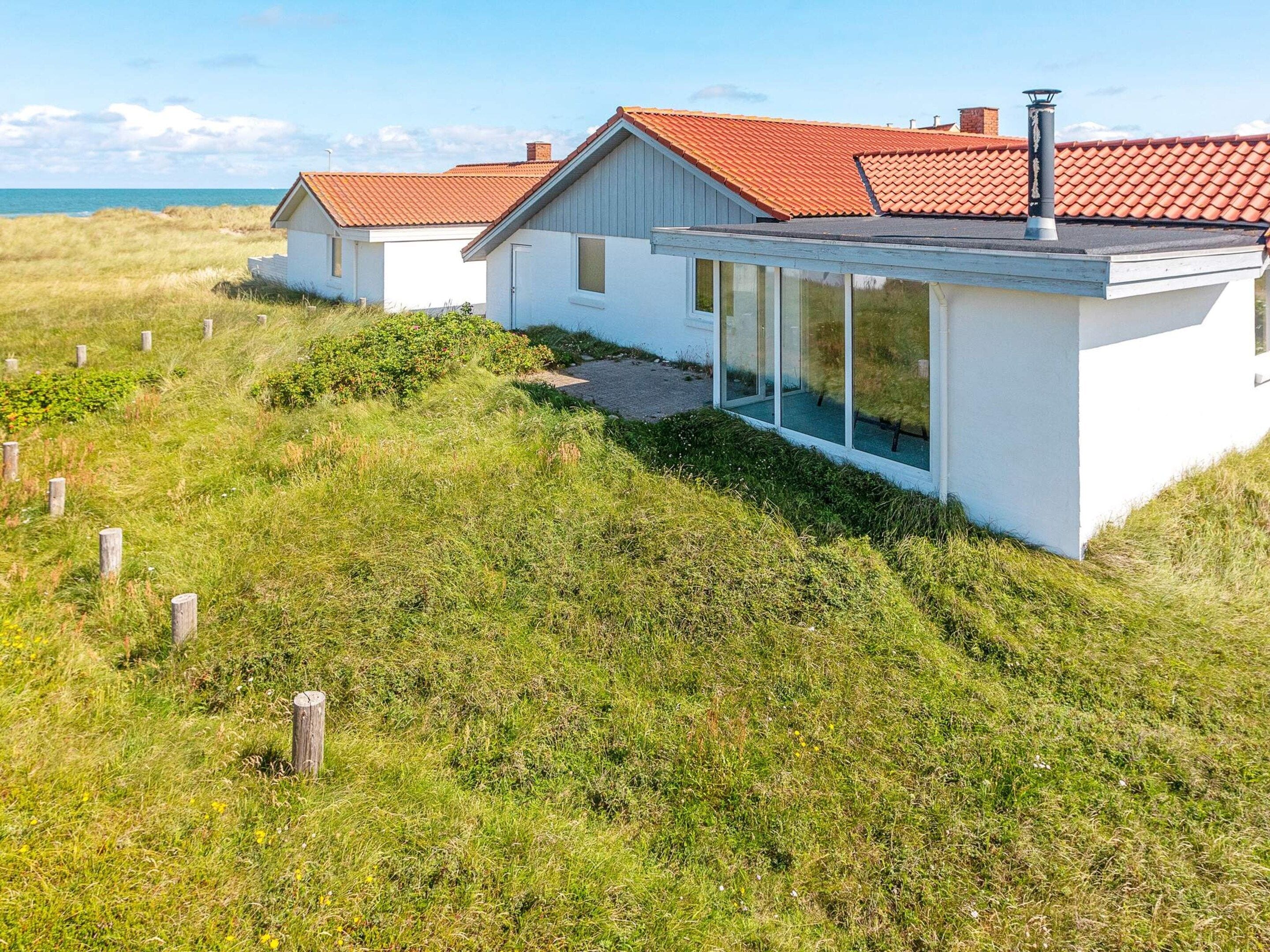 Moderni talo, jossa on punatiilinen katto, suuret ikkunat ja vehreä piha.