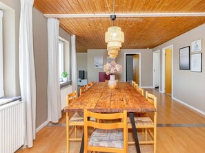 A dining area with a long wooden table, chairs, a hanging light fixture, and a vase with flowers. - 8 Person Holiday Home in Frostrup-by Traum (Frøstrup)
