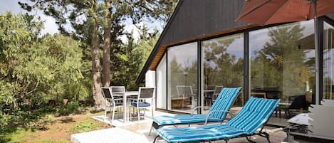 A modern outdoor seating area with lounge chairs and a table, surrounded by glass walls and a dark building facade.