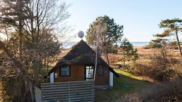 A small wooden cabin with a thatched roof, surrounded by trees and a grassy field.