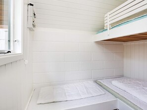 Une petite chambre blanche, avec un lit simple, une fenêtre, des murs blancs et un lit superposé en haut.