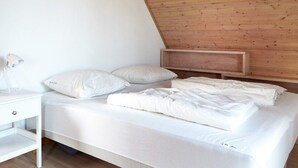 A bedroom with a sloped ceiling, a bed with white bedding, a bedside table, and a lamp. - 12 Person Holiday Home in Sjaellands Odde-by Traum (Sjællands Odde)
