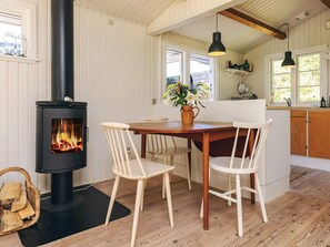 A cozy room with a wood-burning stove, a dining table with chairs, a kitchen area, and a window with a view. - 6 Person Holiday Home in Gilleleje-by Traum (Gilleleje)