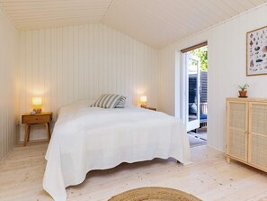A bedroom with a bed, two bedside tables with lamps, a wooden cabinet, and a door leading outside. - 6 Person Holiday Home in Gilleleje-by Traum (Gilleleje)