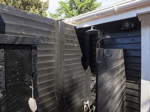 Un mur extérieur en bois noir, avec une gouttière blanche et une porte en métal.