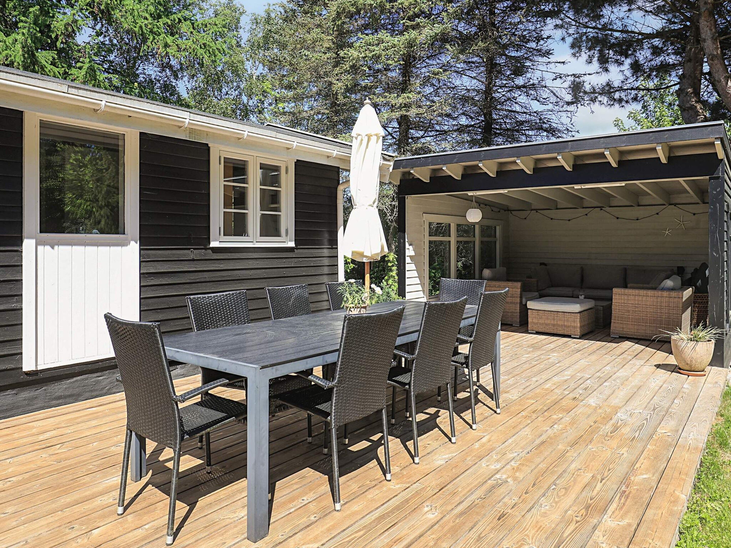 A wooden deck with a dining table and chairs, a covered seating area, and a small house with a white door and windows.