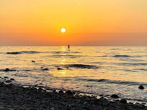 Un coucher de soleil sur une plage rocheuse, avec des vagues et une personne debout dans l’eau.