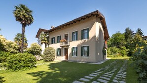 A two-story house with a balcony, surrounded by well-maintained lawns and a variety of trees. - Beautiful private villa for 5 people with WIFI, A/C and patio (San Daniele Del Friuli)
