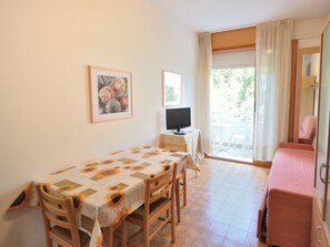 Um quarto pequeno e bem iluminado com uma mesa de jantar, cadeiras, uma televisão e um sofá.