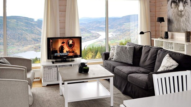 A modern living room with a large TV, comfortable seating, a coffee table, and a scenic view of mountains and a river. - 11 Person Holiday Home in Oyer (Øyer)