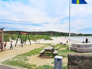 A beach with a swing set, picnic tables, and a flagpole. - Holiday Home in Stråvalla (Stråvalla)