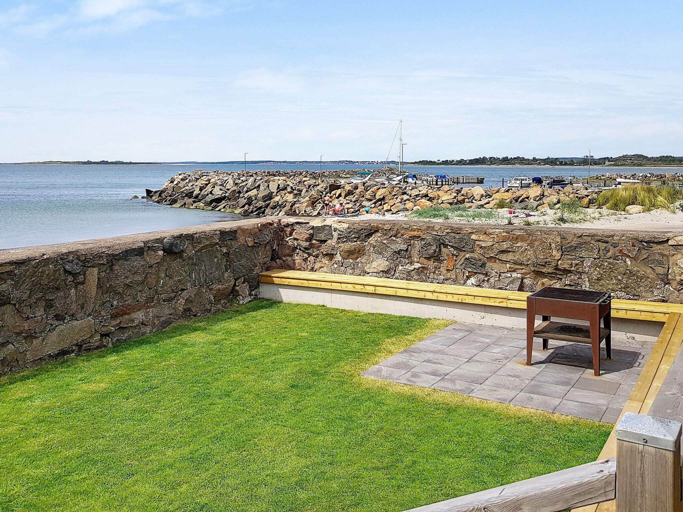 A patio area with a stone wall, a grassy lawn, and a wooden bench.