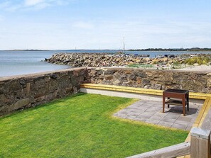 Un patio con muro de piedra, césped y banco de madera.