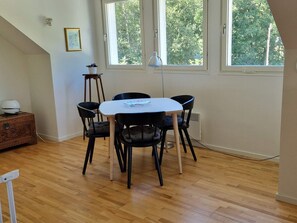 Un comedor con una mesa blanca y cuatro sillas negras, un taburete pequeño y un mueble de madera.