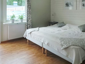 A bedroom with a bed, a radiator, two potted plants, a window with curtains, and a wall with framed pictures. - Holiday Home in Stråvalla (Stråvalla)
