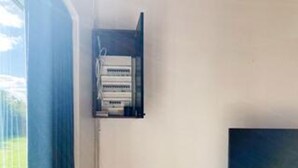 Una stanza con una finestra, un quadro elettrico a parete e un televisore.
