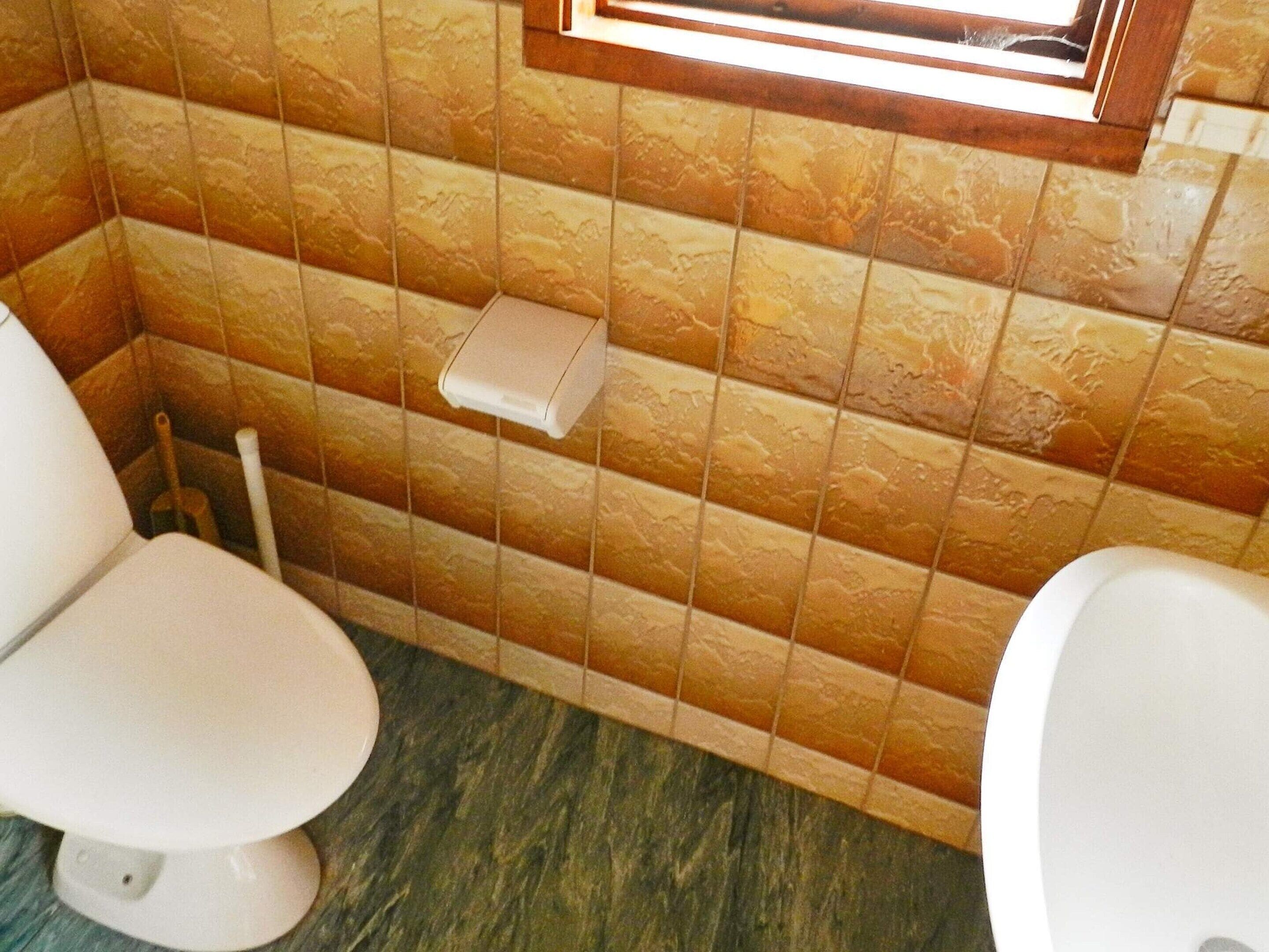 A bathroom with two toilets, a hand dryer, and a window above the sink.