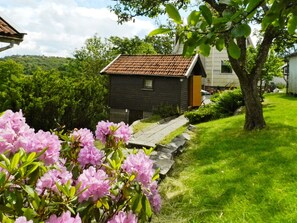 A house with a red-tiled roof, surrounded by a well-maintained garden with pink flowers and a stone pathway leading to the entrance. - 6 Person Holiday Home in Brastad (Brastad)