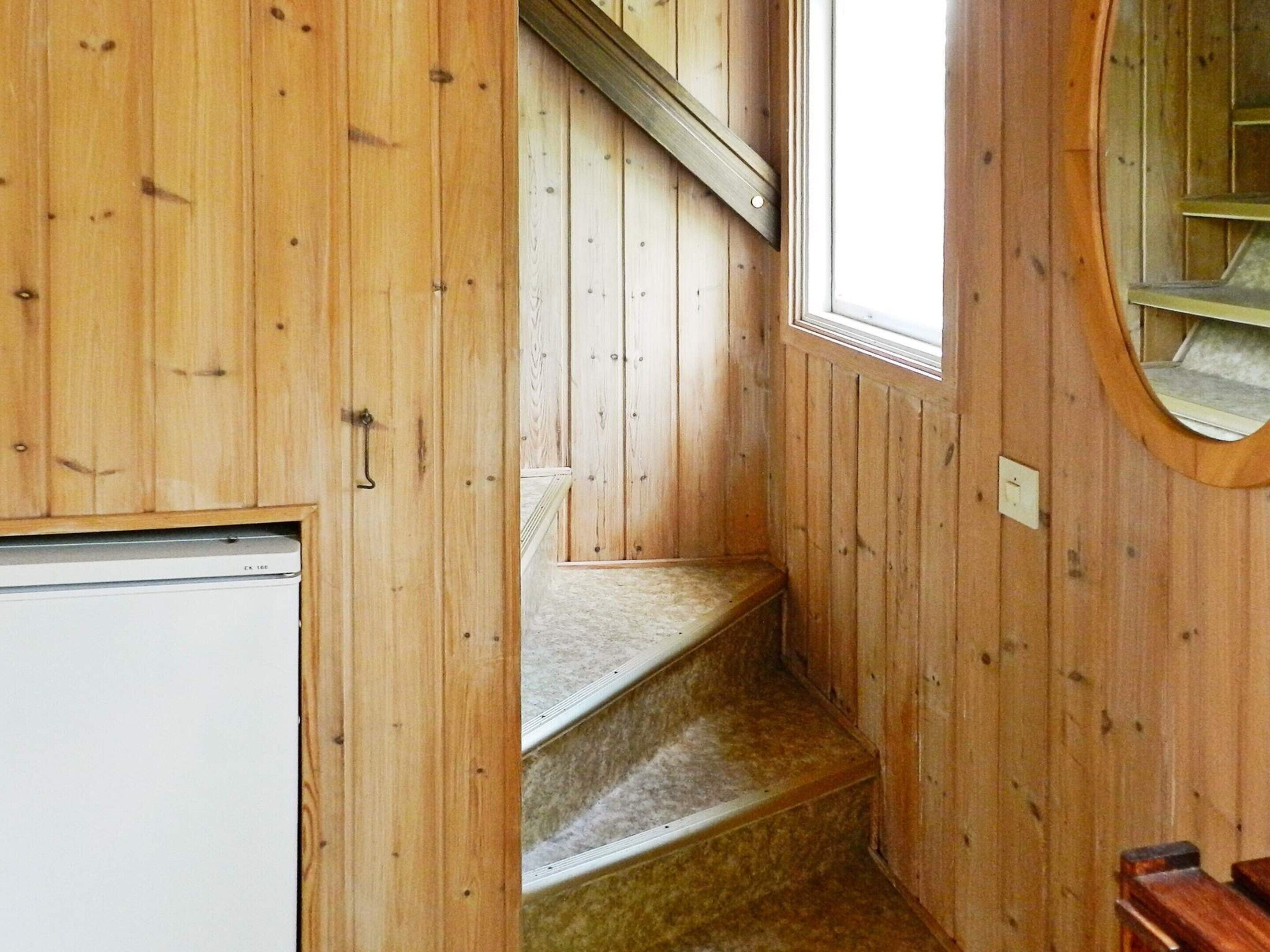 A wooden interior with a staircase, a small window, and a door.