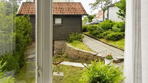 A view through a window of a house with a stone wall, a small garden, and a pathway. - 6 Person Holiday Home in Brastad (Brastad)