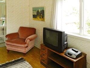 A room with a pink armchair, a television on a wooden stand, and a painting on the wall.