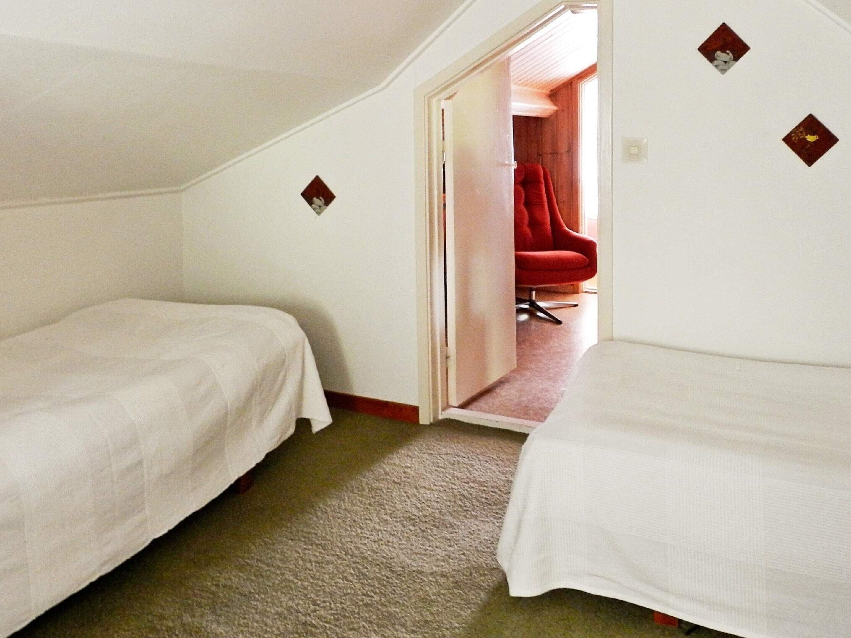 A small, single-room hotel room with two beds, a carpeted floor, and a red chair in the corner.