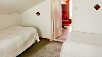 A small, single-room hotel room with two beds, a carpeted floor, and a red chair in the corner.