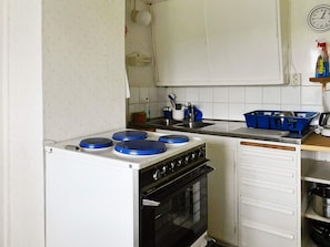 A compact kitchen with a stove, oven, and a sink. There are cabinets and a clock on the wall. - 6 Person Holiday Home in Brastad (Brastad)