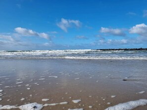 A beach with waves, a clear sky, and a distant rocky shoreline. - 5 Star Holiday Home in Frederiksvaerk (Frederiksvaerk)