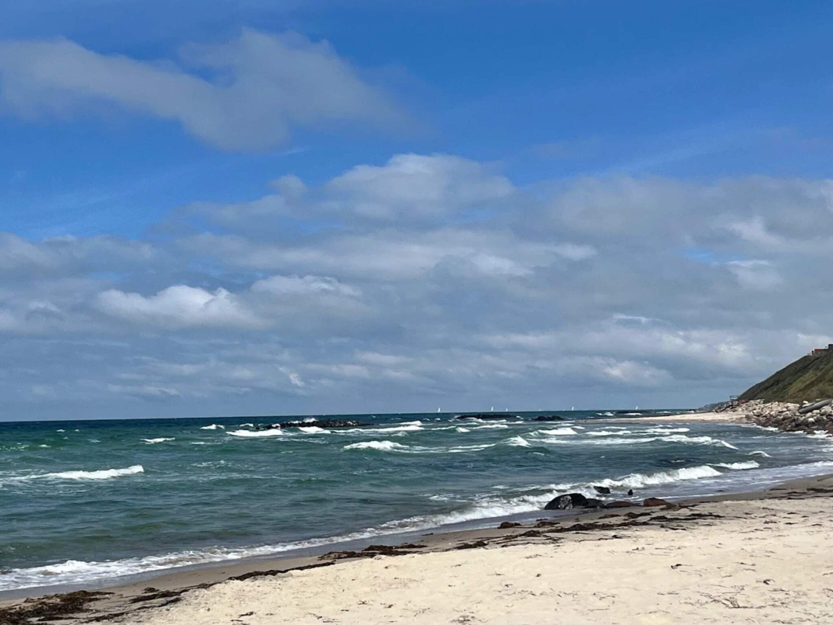 Una spiaggia con onde, cielo sereno e un promontorio roccioso.