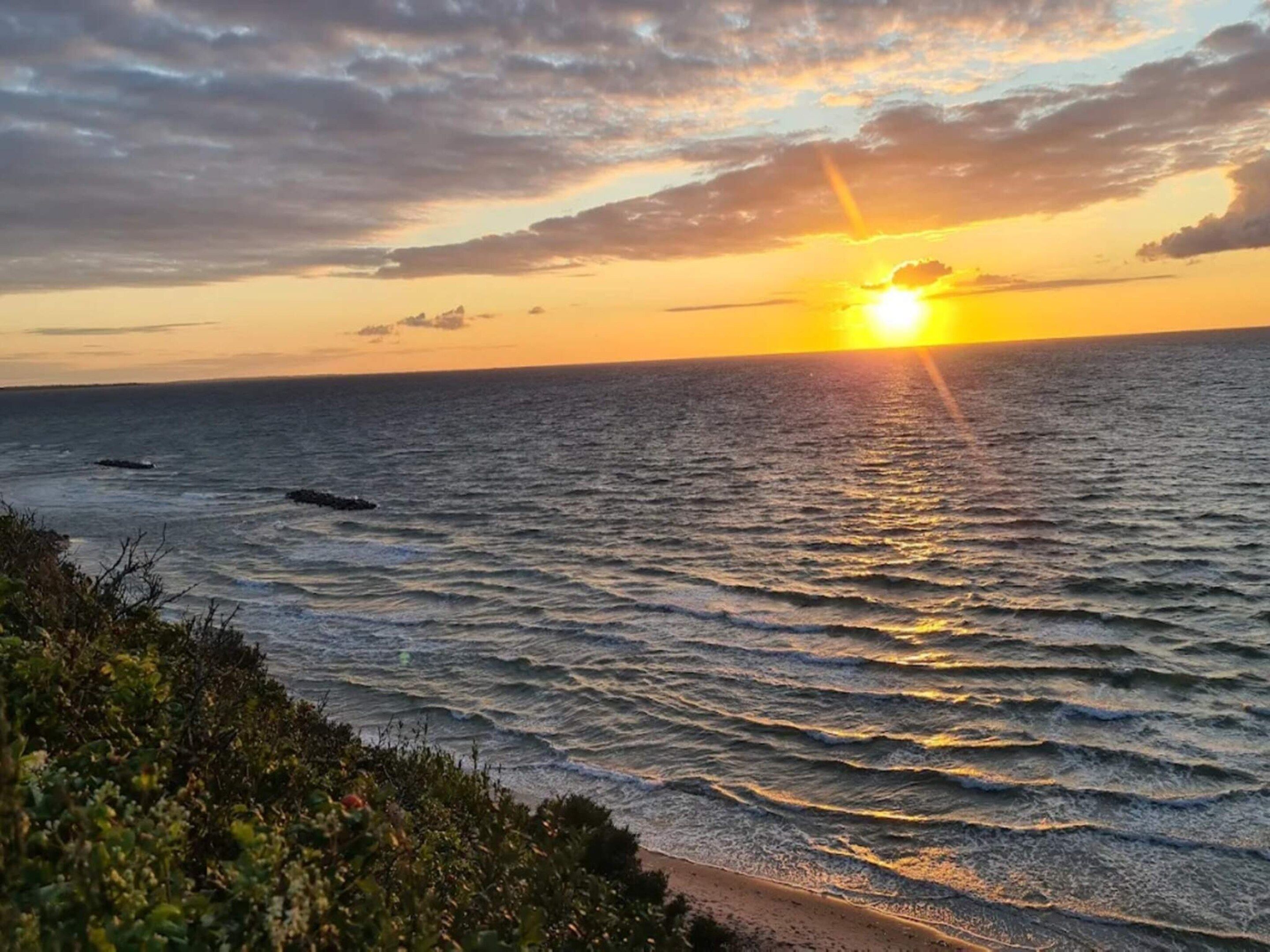 A sunset over the ocean with waves and a beach in the foreground.