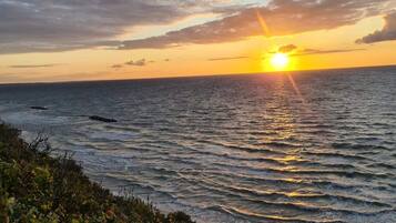 A sunset over the ocean with waves and a beach in the foreground.
