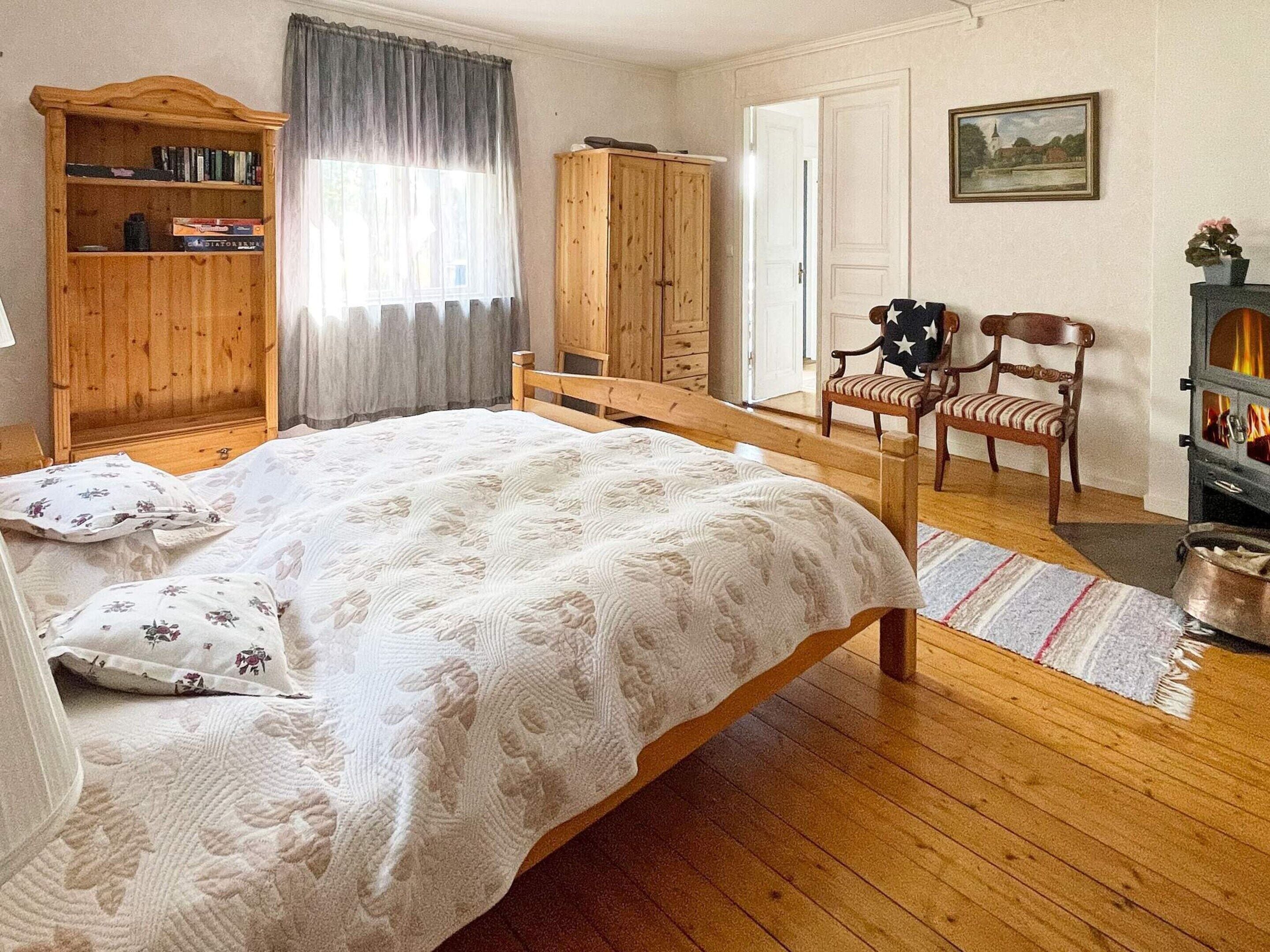 Ein Schlafzimmer mit einem hölzernen Bett, einem Kleiderschrank, einem Stuhl, einem kleinen Tisch und einem Bild an der Wand.