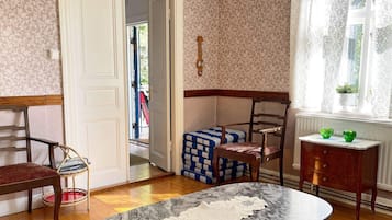 A room with a marble table, a wooden chair, a bench with cushions, a small wooden cabinet, and a door leading outside.