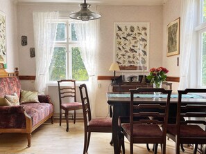 A cozy living room with a sofa, chairs, a dining table, and a large window with a view of greenery. - 4 Star Holiday Home in Orsjo (Örsjö)