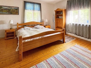 A wooden bed in a room with a painting, a nightstand, a wooden cabinet, and a window with curtains. - 4 Star Holiday Home in Orsjo (Örsjö)