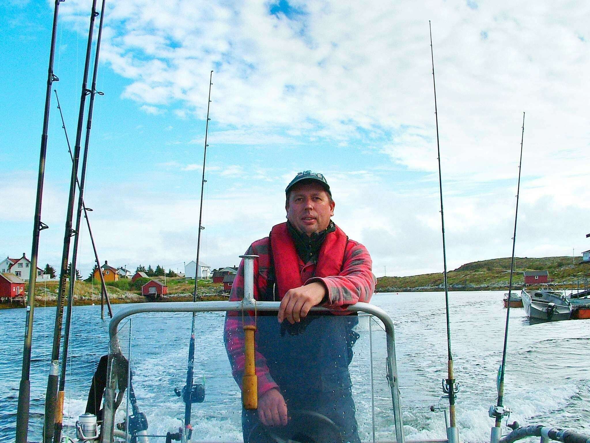 A person on a boat with fishing rods, surrounded by water and houses in the background.