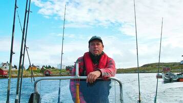 A person on a boat with fishing rods, surrounded by water and houses in the background.