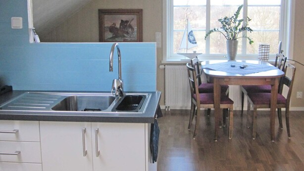 A kitchen with a double sink, a dining table with chairs, and a window with a view of trees. - 4 Person Holiday Home in Romelanda (Romelanda)