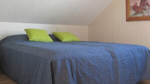 A single bed with a blue bedspread and two green pillows in a room with a sloped ceiling and a framed painting on the wall. - 4 Person Holiday Home in Romelanda (Romelanda)